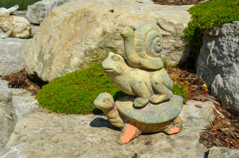 Garden snail ornament beside limestone boulders, clipped groundcover, mulch, and shrubs.